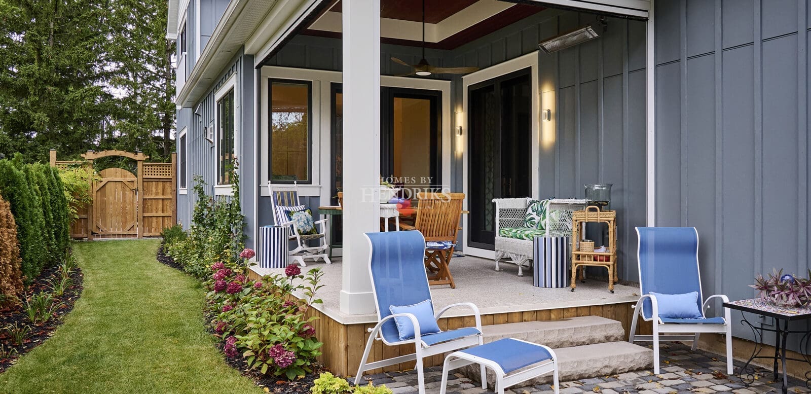 Exterior view of a dining space featuring teak outdoor furniture and an exterior heater, set against a backdrop of grey Hardie board and batten siding, creating a cozy and stylish outdoor atmosphere.