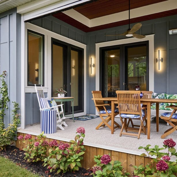 Exterior view of a dining area showcasing teak outdoor furniture and an exterior heater, framed by grey Hardie board and batten siding, emphasizing a comfortable and inviting outdoor setting.