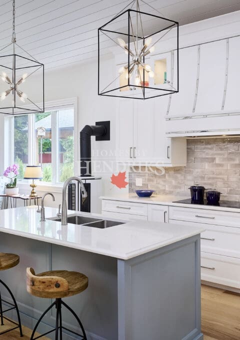 Interior view of the kitchen highlighting the central island, surrounded by white cabinetry, an induction range, and a brick backsplash, creating a spacious and functional cooking area.