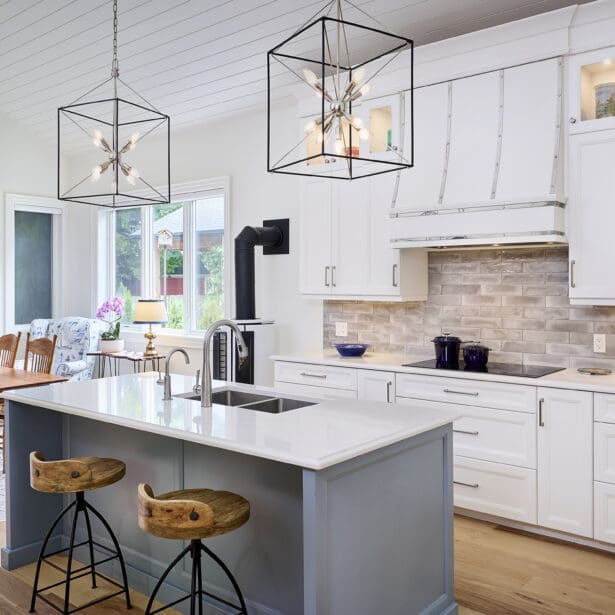 Interior view of the kitchen highlighting the central island, surrounded by white cabinetry, an induction range, and a brick backsplash, creating a spacious and functional cooking area.