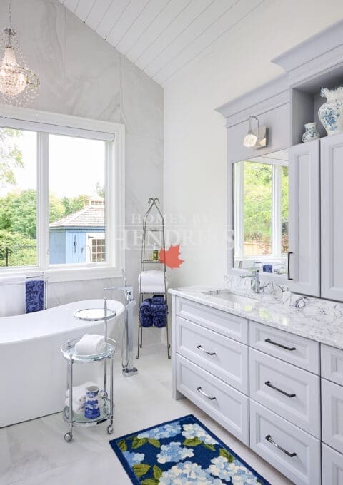 Interior view of a primary ensuite bathroom featuring grey cabinetry, a freestanding soaker tub, and a vaulted ceiling, combining elegance and comfort.