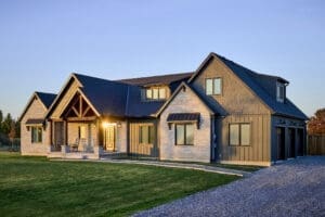 The front elevation of the home showcases a harmonious blend of Hardie board and batten siding with Hardie shake accents, creating a timeless yet contemporary look. Custom Douglas fir timber framing adds warmth and character, while natural stone masonry enhances the rustic charm.