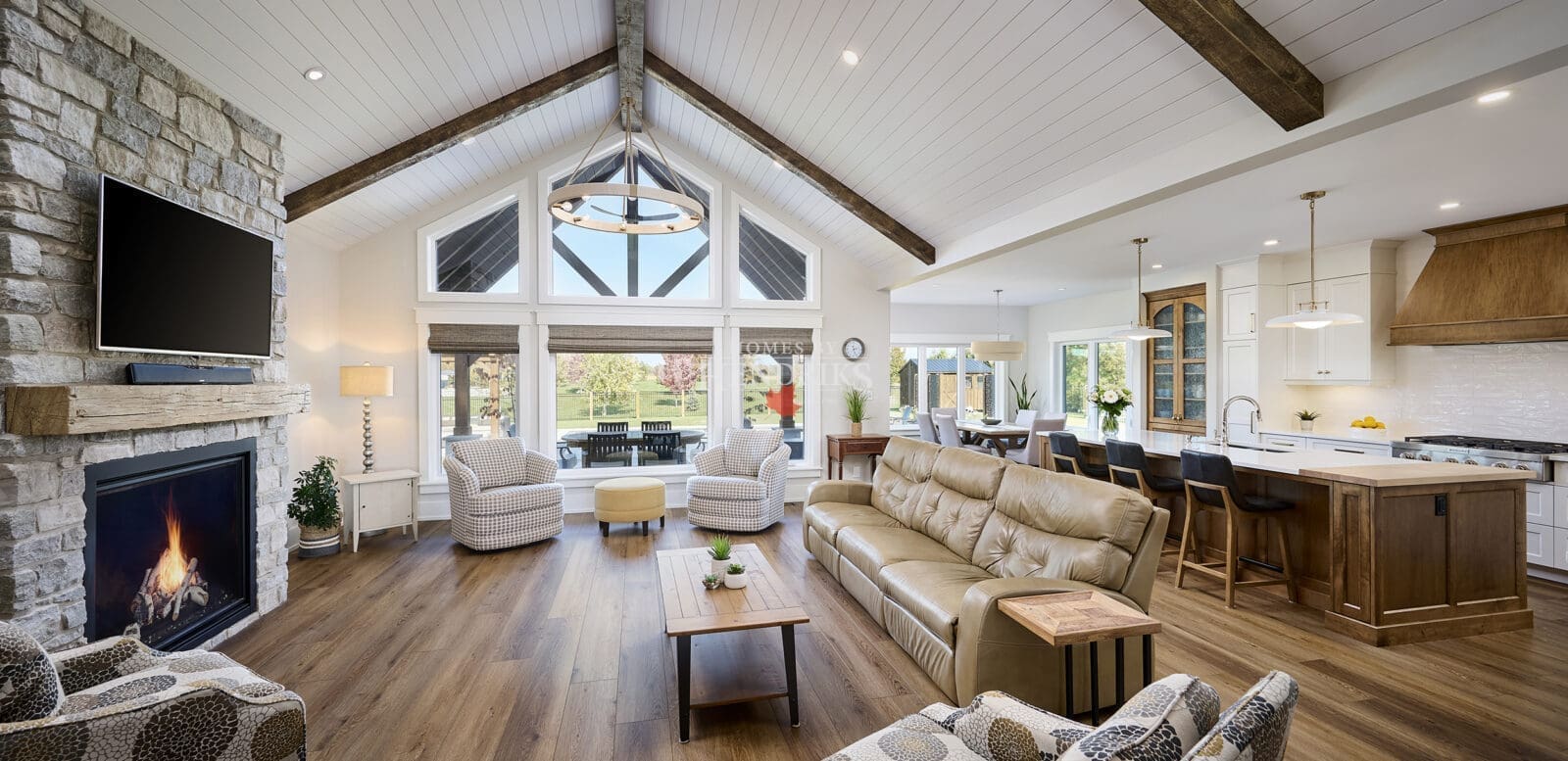 A grand great room featuring stunning timber accents that add warmth and rustic charm to the space. The high ceilings are framed by exposed wooden beams, while large windows allow natural light to flood the room