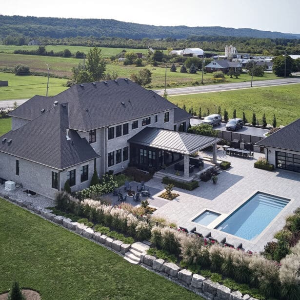 Refined custom home with a rich stone exterior and limestone detailing, complemented by a lush garden and sparkling pool.