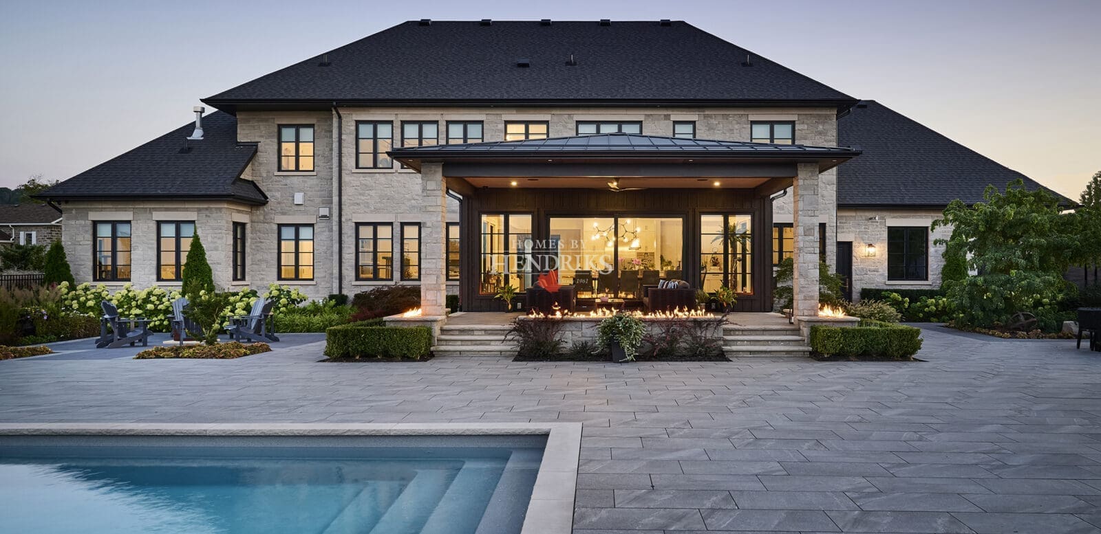 Elegant custom home with a beautiful stone exterior, limestone accents, and a stunning pool area surrounded by lush landscaping.