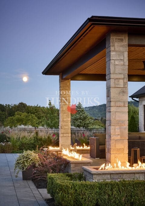 Gorgeous custom residence featuring a stone exterior, limestone highlights, and a pristine pool with lush greenery.