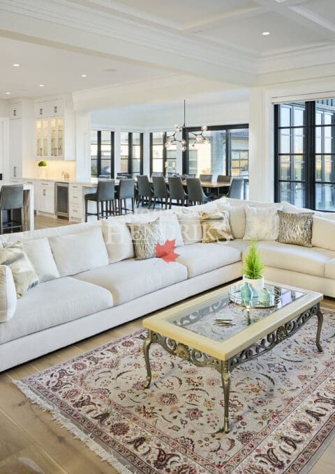 Bright, open-concept kitchen and dining area featuring a large waterfall-edge island, pendant lighting, white cabinetry, wide-plank hardwood floors, and expansive windows overlooking the backyard.