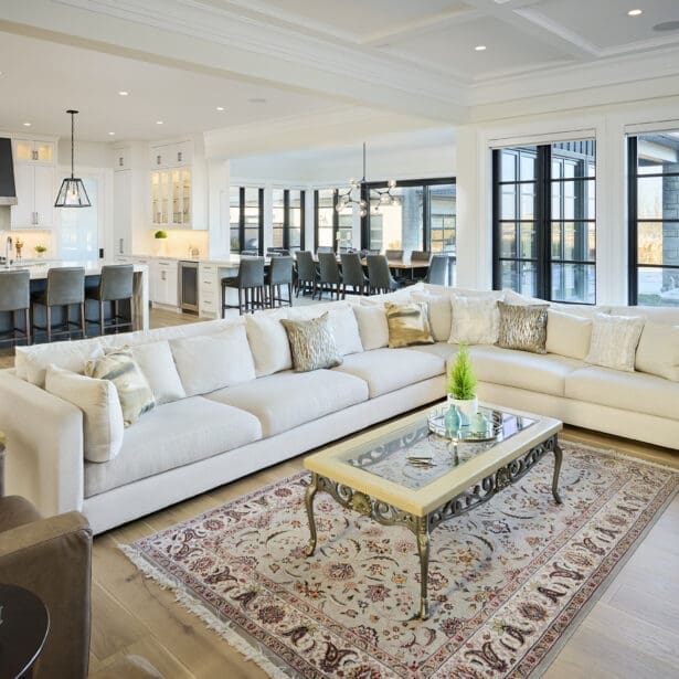 Bright, open-concept kitchen and dining area featuring a large waterfall-edge island, pendant lighting, white cabinetry, wide-plank hardwood floors, and expansive windows overlooking the backyard.