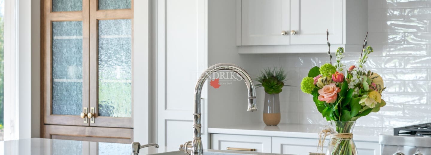 A beautiful kitchen featuring custom two-tone maple cabinetry, blending natural wood tones with a modern finish. The space is complemented by rustic timber beams and ample natural light, creating a warm, inviting atmosphere.