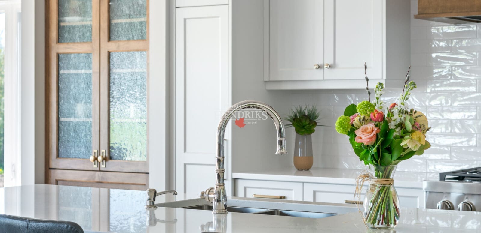 A beautiful kitchen featuring custom two-tone maple cabinetry, blending natural wood tones with a modern finish. The space is complemented by rustic timber beams and ample natural light, creating a warm, inviting atmosphere.