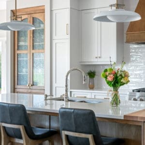 A beautiful kitchen featuring custom two-tone maple cabinetry, blending natural wood tones with a modern finish. The space is complemented by rustic timber beams and ample natural light, creating a warm, inviting atmosphere.