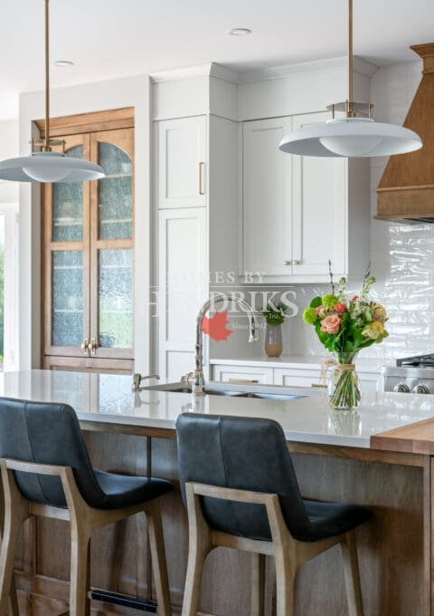A beautiful kitchen featuring custom two-tone maple cabinetry, blending natural wood tones with a modern finish. The space is complemented by rustic timber beams and ample natural light, creating a warm, inviting atmosphere.