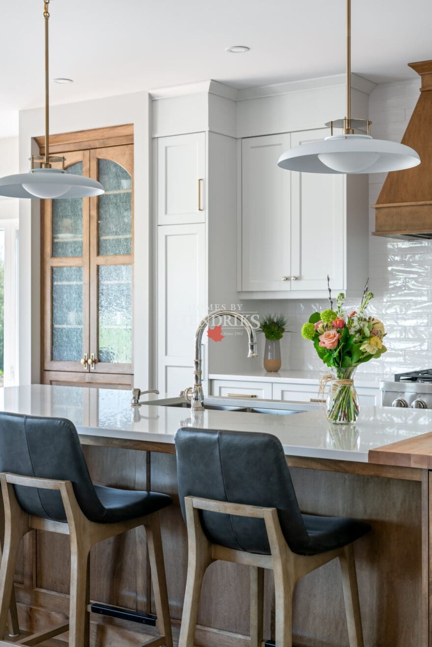 A beautiful kitchen featuring custom two-tone maple cabinetry, blending natural wood tones with a modern finish. The space is complemented by rustic timber beams and ample natural light, creating a warm, inviting atmosphere.