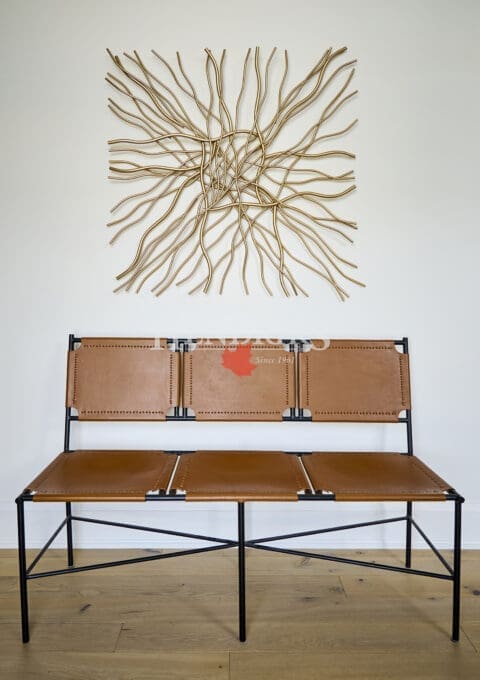 Minimalist hallway wall featuring a geometric gold metal art installation above a modern leather bench with black metal frame and stitched tan seats