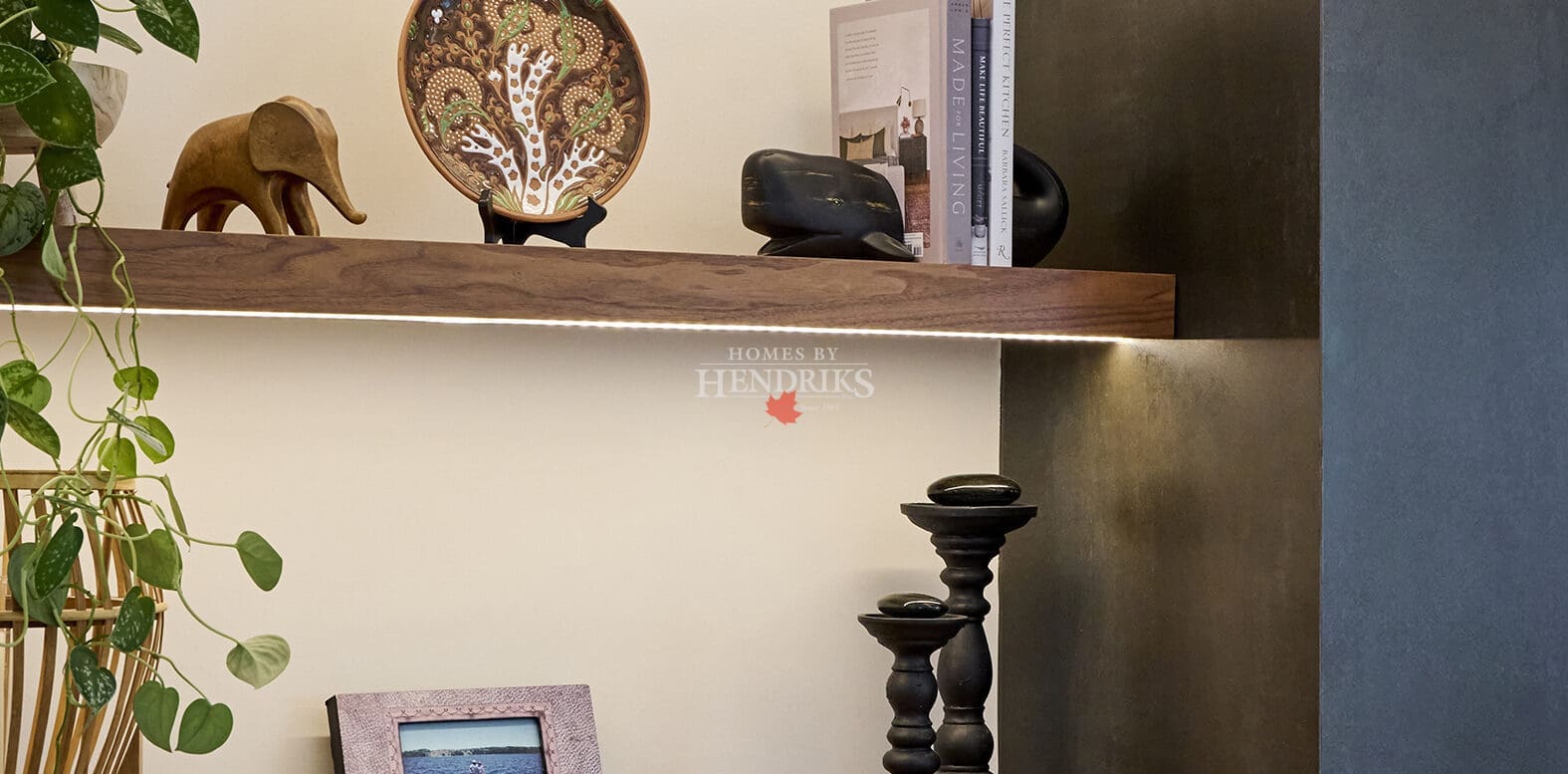 Detail of built-in shelving displaying books, ceramics, and decorative art pieces, accented by warm wood cabinetry and integrated lighting.