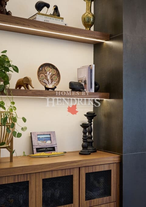 Detail of built-in shelving displaying books, ceramics, and decorative art pieces, accented by warm wood cabinetry and integrated lighting.