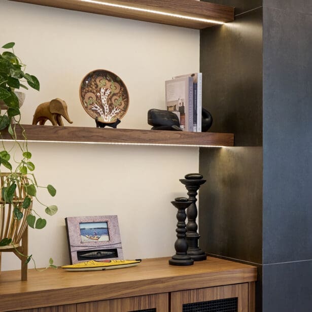 Detail of built-in shelving displaying books, ceramics, and decorative art pieces, accented by warm wood cabinetry and integrated lighting.