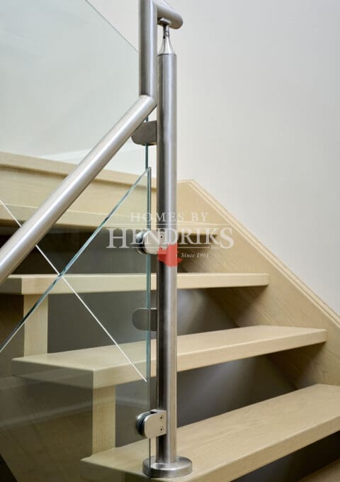 Close-up of contemporary glass stair railing with stainless steel posts and hardware detailing, showcasing craftsmanship and precision joinery