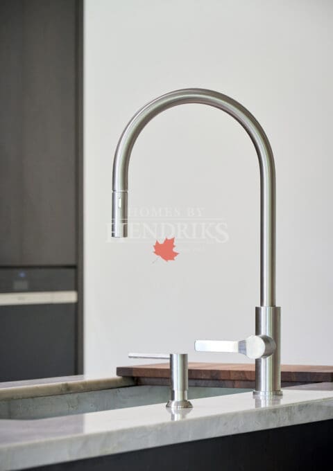 Close-up of a sleek brushed-steel kitchen faucet with pull-down sprayer, set against a minimalist marble countertop and dark cabinetry background