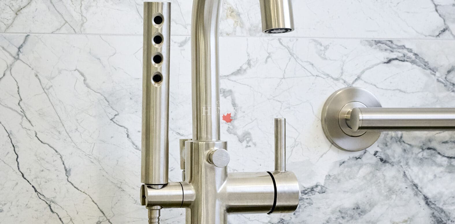 Close-up of brushed nickel bathtub faucet and handheld sprayer mounted on marble wall above a sculptural freestanding tub.