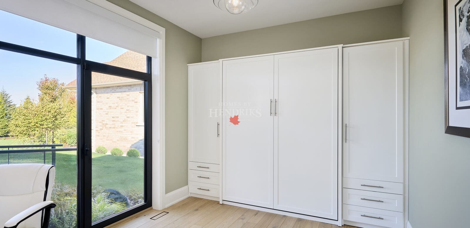 Bright mudroom with floor-to-ceiling white cabinetry, light wood floors, and a minimalist glass pendant light beside a large window