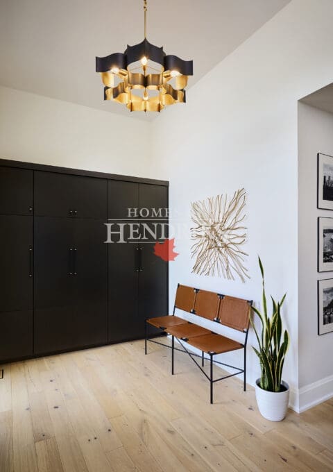 Modern mudroom with custom black cabinetry, tan leather bench seating, gold geometric chandelier, and wall art with metallic branch design.