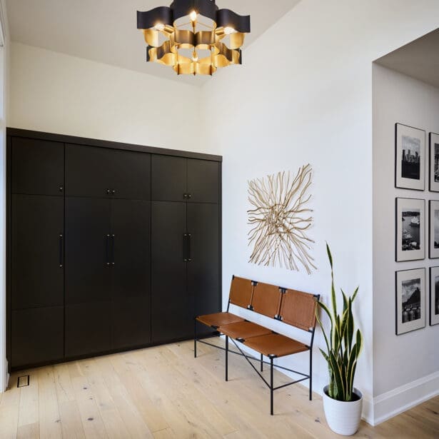 Modern mudroom with custom black cabinetry, tan leather bench seating, gold geometric chandelier, and wall art with metallic branch design.