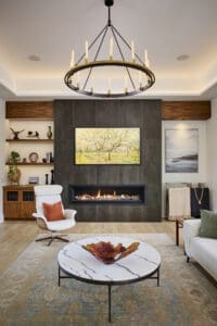 Contemporary living room with floor-to-ceiling tiled fireplace, circular chandelier, and modern lounge seating. Features a marble coffee table, decorative art, and built-in shelving with wood finishes.