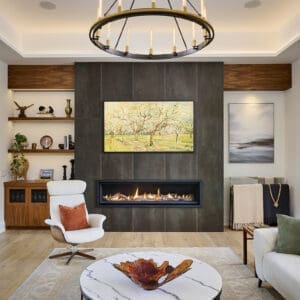 Contemporary living room with floor-to-ceiling tiled fireplace, circular chandelier, and modern lounge seating. Features a marble coffee table, decorative art, and built-in shelving with wood finishes.