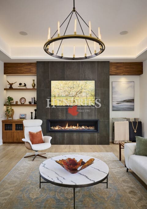 Contemporary living room with floor-to-ceiling tiled fireplace, circular chandelier, and modern lounge seating. Features a marble coffee table, decorative art, and built-in shelving with wood finishes.