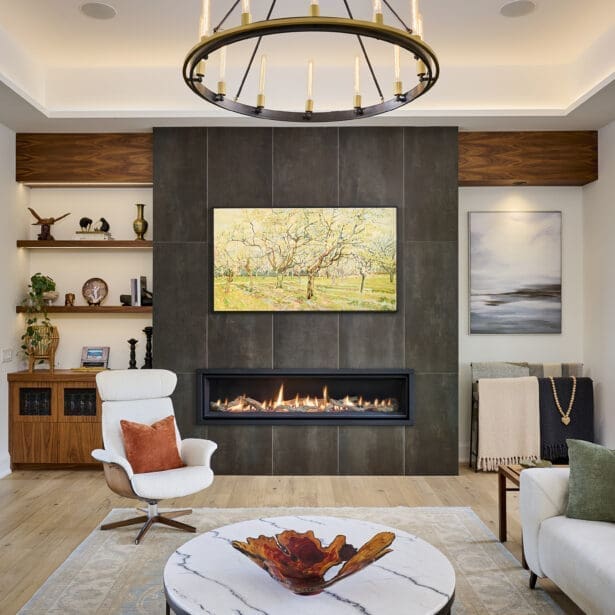 Contemporary living room with floor-to-ceiling tiled fireplace, circular chandelier, and modern lounge seating. Features a marble coffee table, decorative art, and built-in shelving with wood finishes.