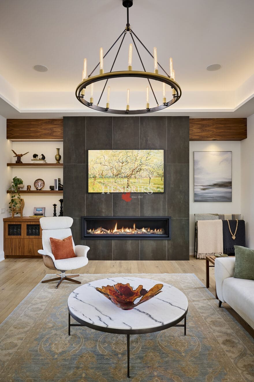 Contemporary living room with floor-to-ceiling tiled fireplace, circular chandelier, and modern lounge seating. Features a marble coffee table, decorative art, and built-in shelving with wood finishes.