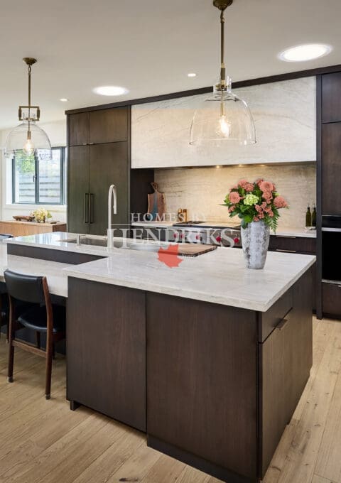 Modern open-concept kitchen and dining area featuring dark wood cabinetry, marble countertops, and large glass doors opening to an outdoor patio. Pendant lighting and floral accents add warmth and sophistication