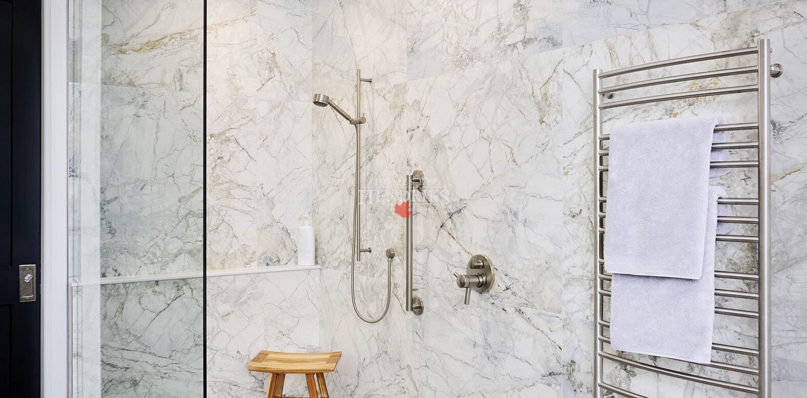 Spacious walk-in shower with marble walls, rain shower head, handheld sprayer, and towel warmer. Includes accessibility features and a small wooden bench