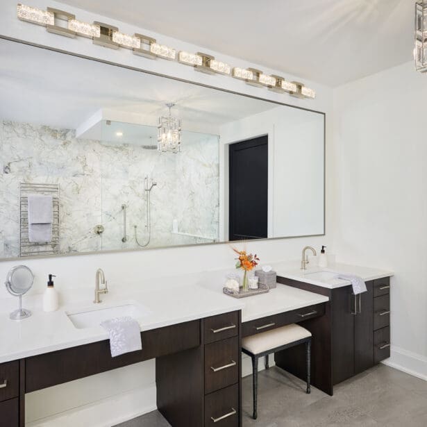 Luxury bathroom with dual vanities, white quartz countertops, and dark wood cabinetry. Large illuminated mirror and marble shower enclosure with glass walls