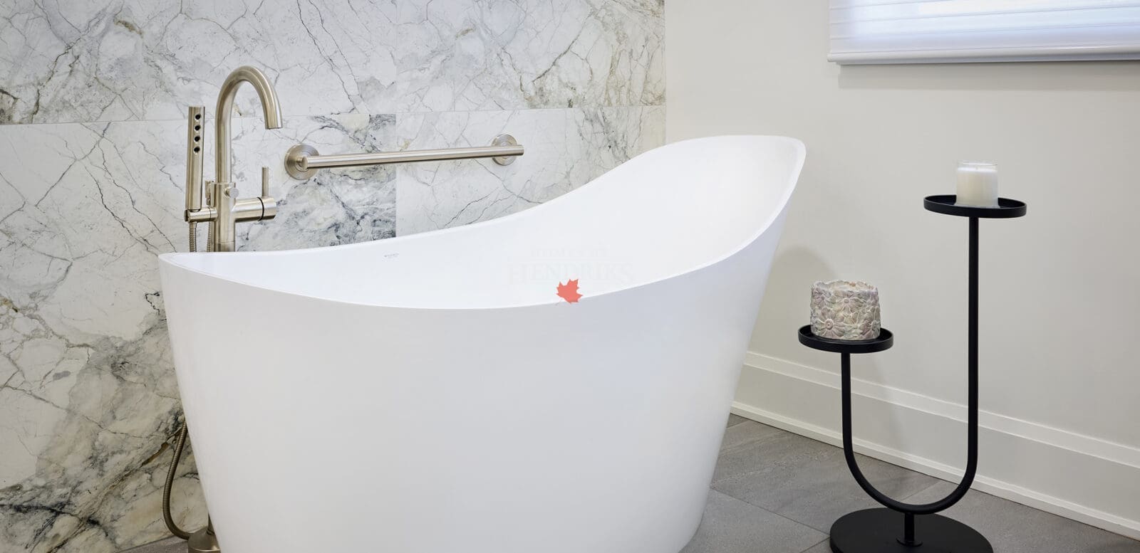 Elegant freestanding white bathtub with brushed nickel faucet, marble accent wall, and minimalist black candle stand for spa-like ambiance.