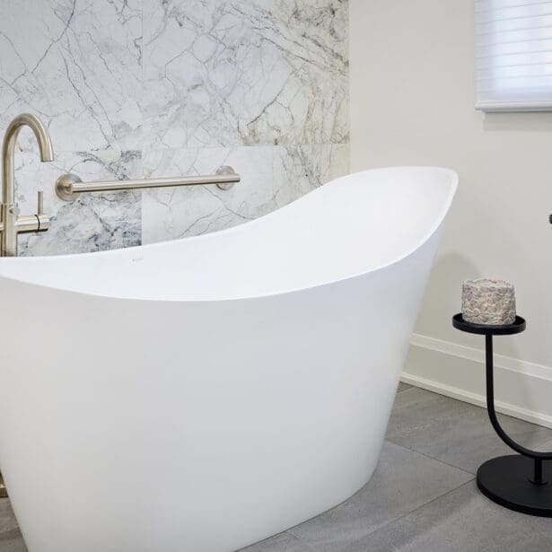Elegant freestanding white bathtub with brushed nickel faucet, marble accent wall, and minimalist black candle stand for spa-like ambiance.