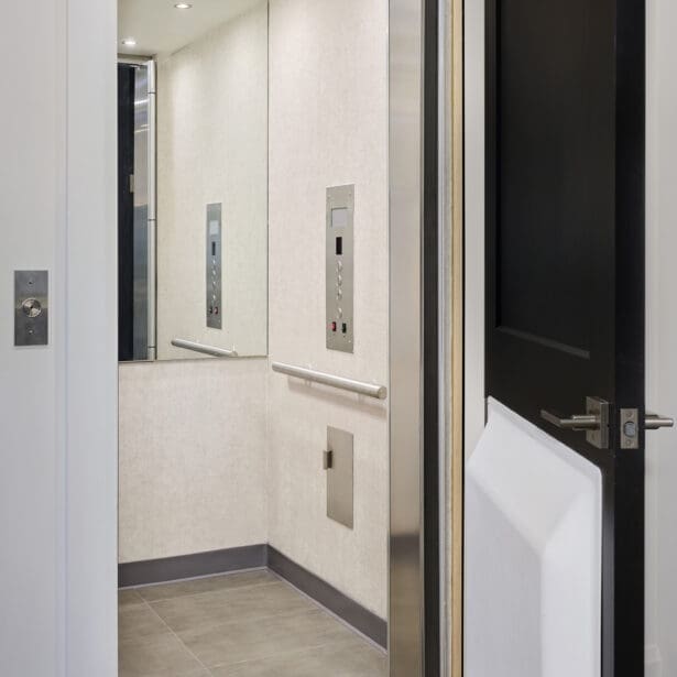 Residential elevator with modern stainless steel finishes, mirrored walls, and recessed ceiling lights inside a luxury custom home.