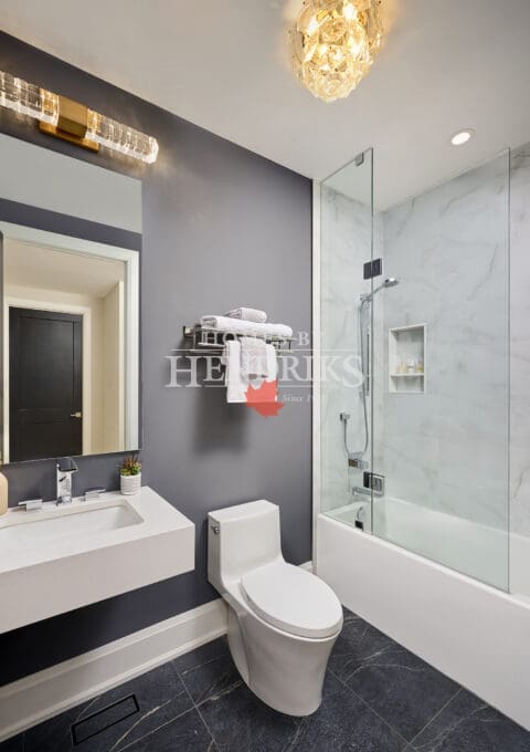 Open-concept living room featuring white sectional sofas, marble coffee table, and circular chandelier. Kitchen and dining area visible in the background