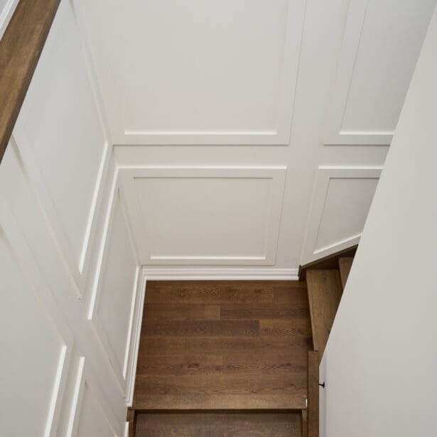 View down a custom stairwell featuring white paneled walls and rich oak treads for a clean, transitional design.