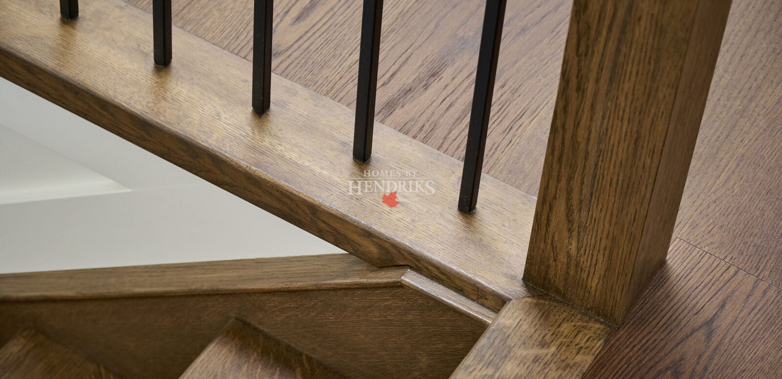 Close-up of custom oak stair railing with black metal balusters, highlighting precise joinery and fine wood craftsmanship.