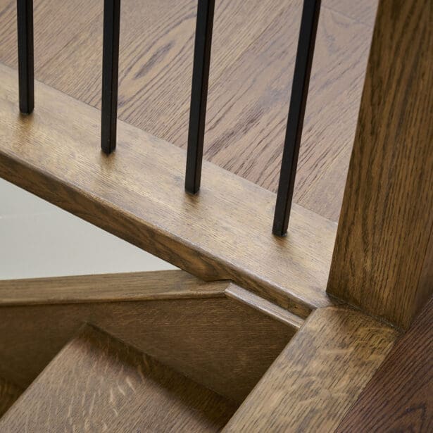 Close-up of custom oak stair railing with black metal balusters, highlighting precise joinery and fine wood craftsmanship.
