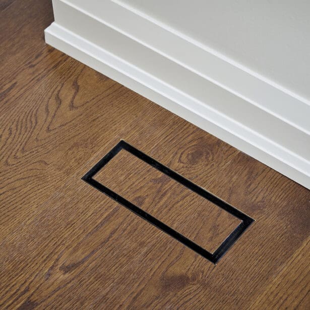 Discreet floor vent integrated seamlessly into oak hardwood flooring with matching trim for a clean architectural finish.