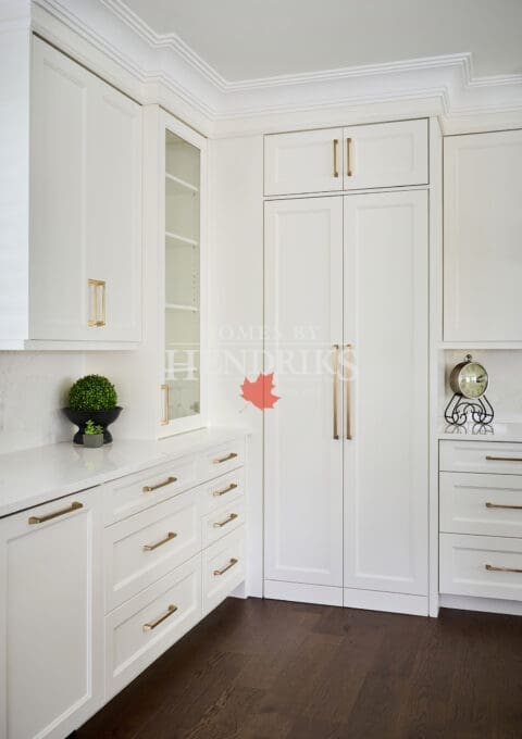 Bright custom kitchen cabinetry with inset doors, brass hardware, integrated fridge panels, and detailed crown moulding design.