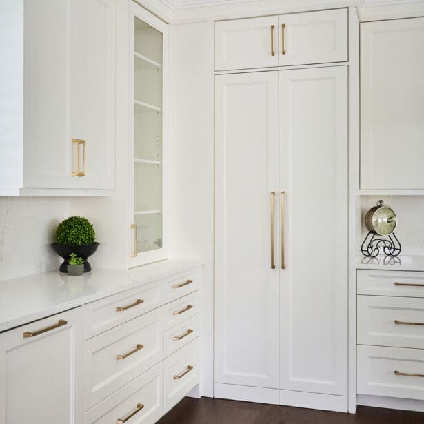 Bright custom kitchen cabinetry with inset doors, brass hardware, integrated fridge panels, and detailed crown moulding design.
