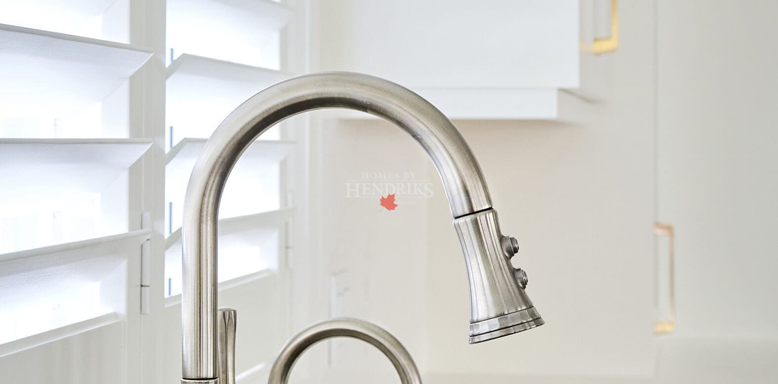 Brushed nickel kitchen faucet and matching prep tap in front of plantation shutters, blending modern function with timeless finishes.