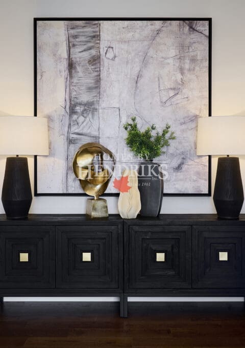 Sophisticated entry vignette featuring a black wood console, abstract wall art, gold sculptural accent, and matching black table lamps with white shades.