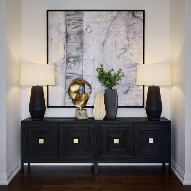 Sophisticated entry vignette featuring a black wood console, abstract wall art, gold sculptural accent, and matching black table lamps with white shades.