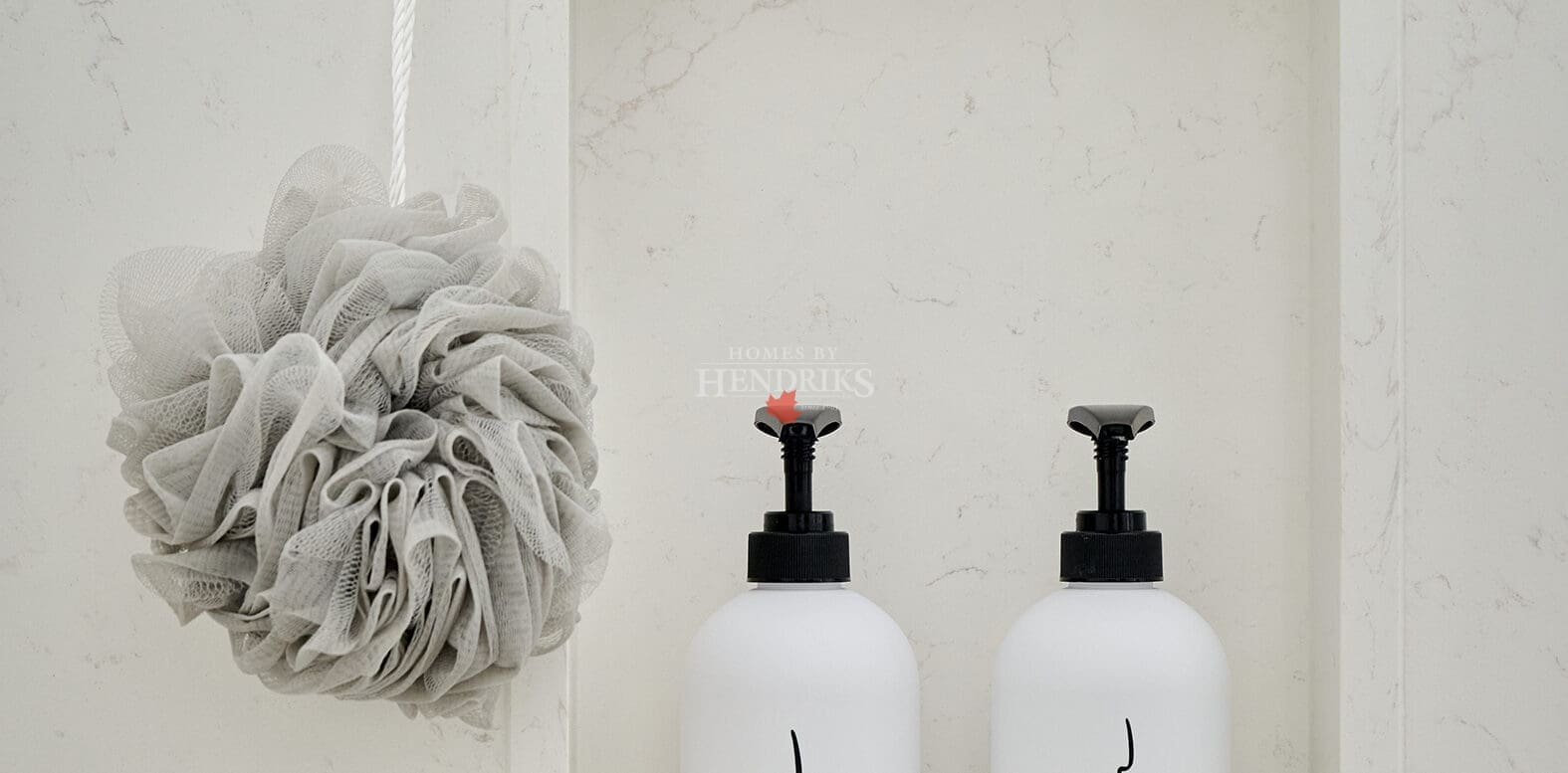 Marble shower niche with labeled white bottles and a neutral bath pouf, styled for a clean and timeless spa aesthetic