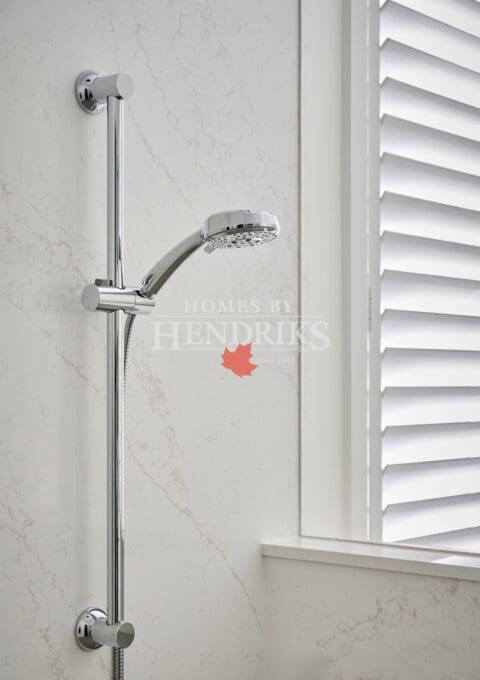 Polished chrome adjustable handheld shower mounted on marble wall with horizontal blinds in the background.